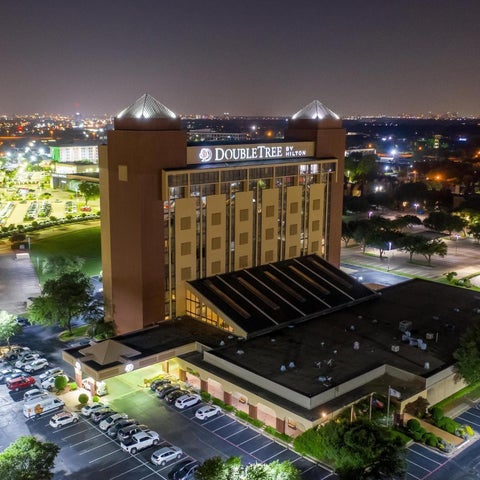An aerial view showcases a DoubleTree hotel with a prominent tower design, surrounded by a parking lot and city lights.