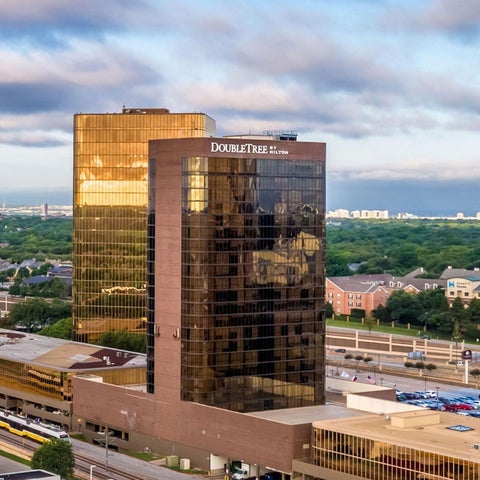 A high-angle view showcases the DoubleTree Hilton hotel with its reflective glass facade and surrounding cityscape.