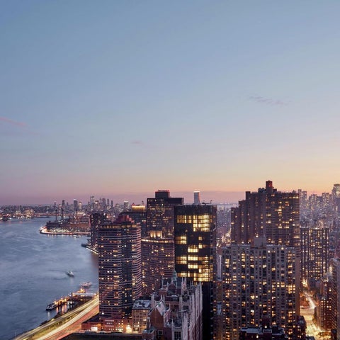 An aerial view showcases the Manhattan skyline at dusk, featuring numerous skyscrapers and the Hudson River.