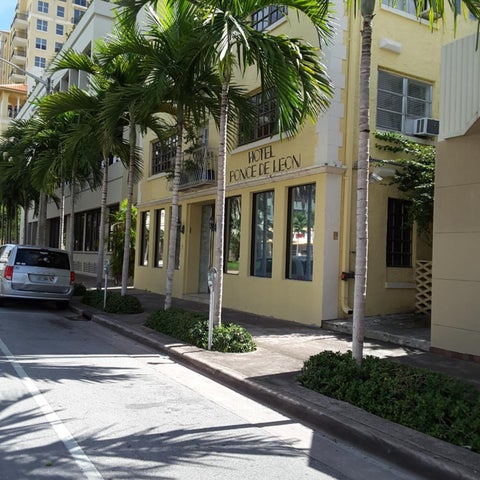 A yellow building, Hotel Fonde de Leon, is seen with palm trees lining the street and a car parked nearby.